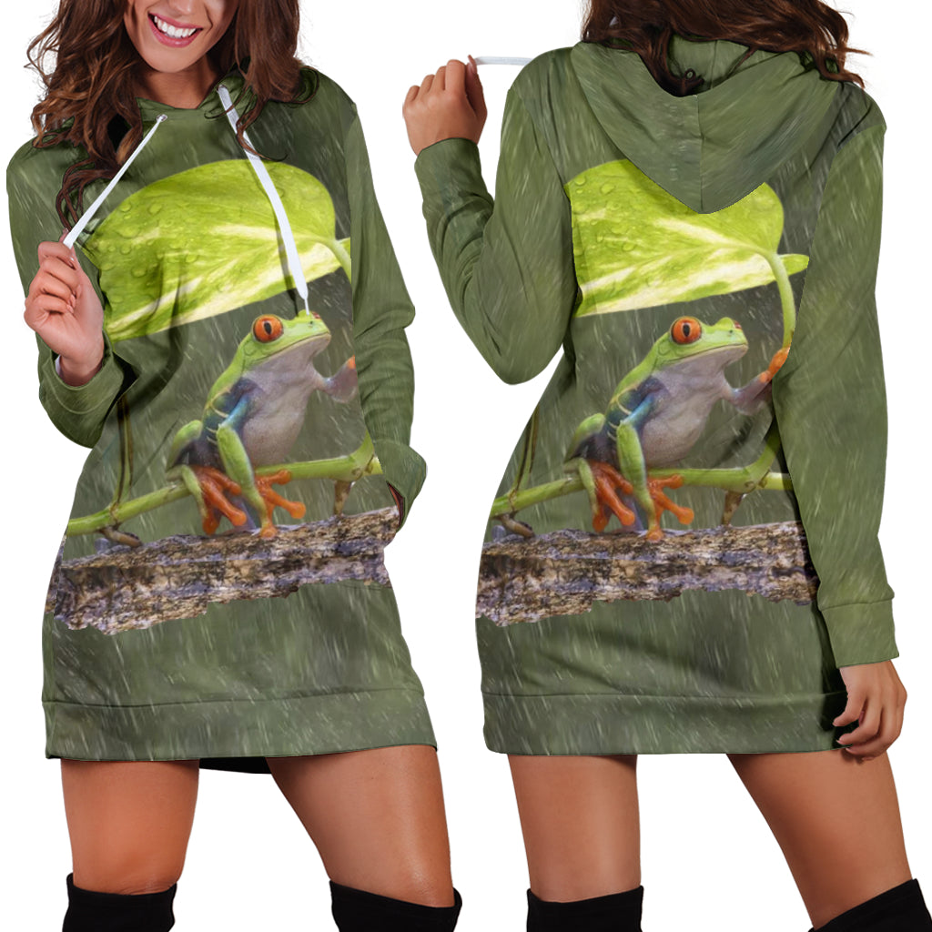 A woman wearing a green hoodie dress with a printed frog on the front, posing with the hood on and a smile on her face.