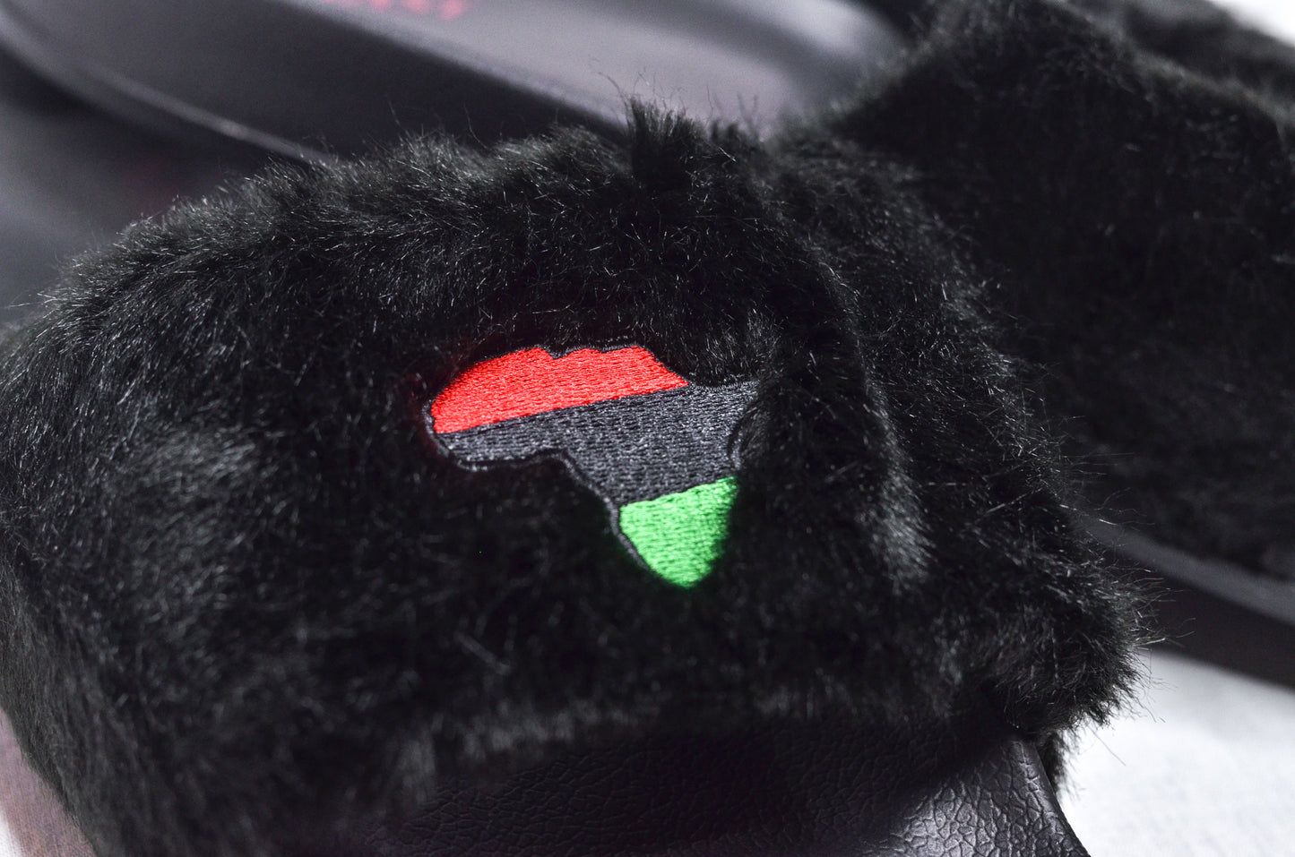  Close-up of Queen Nzinga Empress Black Fur Slippers showing detailed RBG flag embroidery on soft fur strap.